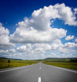 Road toward horizon, fluffy clouds above