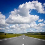 Road toward horizon, fluffy clouds above
