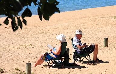 Two people in lawn chairs on a beach, reading