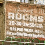 Old sign painted on brick building "Rooms 25 - 50 cents per night, $1.50 per week."