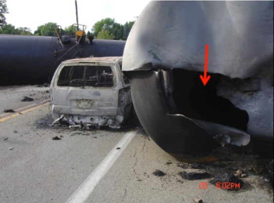A tank car carrying ethanol involved in the Cherry Valley derailment showing head (tank car end ) failure lying next to burned automobile. Arrow points to head failure. (Credit: NTSB)