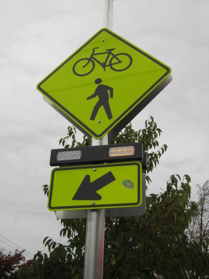 This crosswalk sign helps pedestrians and cyclists cross 24th Avenue NW by flashing when activated.