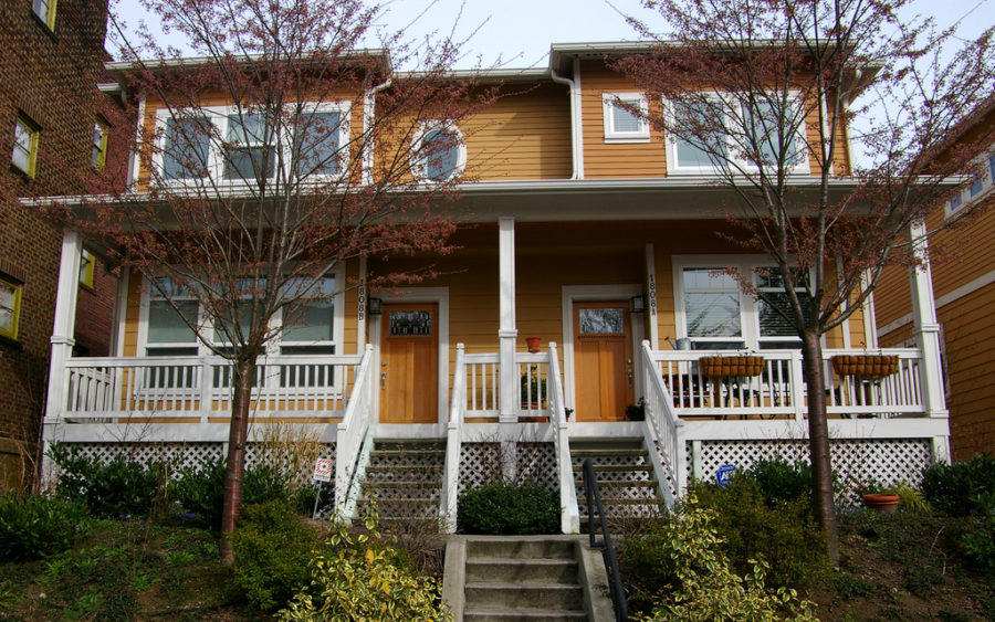 Yellow two-story duplex in Seattle, with stairs to a porch with white wooden railings.