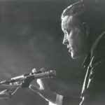 black and white photo of a white man in middle age speaking into a microphone