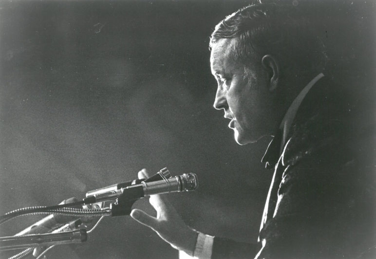 black and white photo of a white man in middle age speaking into a microphone