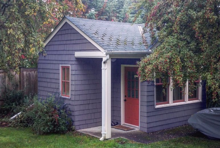 In the photo is a small accessory dwelling home--an example of the kind of backyard homes this policy solution would allow. The view is of a welcoming front door and front stoop and the house is surrounded by green grass and trees.