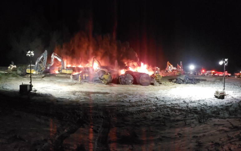 construction equipment and crew working near a number of oil cars on fire, at night