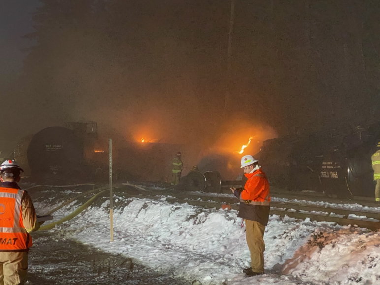 first responders with firehoses next to derailed oil cars at night