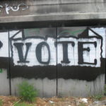 Spray painted banner art on wall: "Vote."