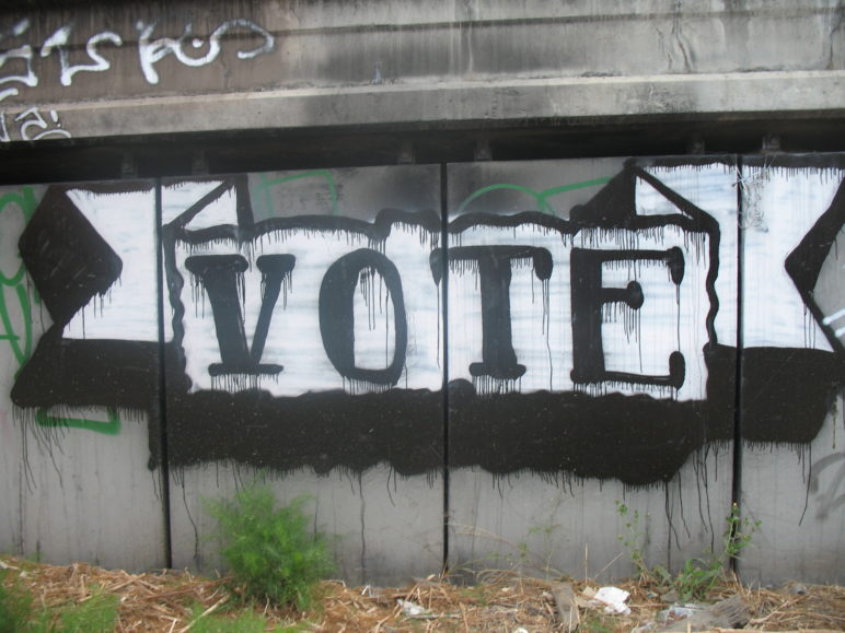 Spray painted banner art on wall: "Vote."