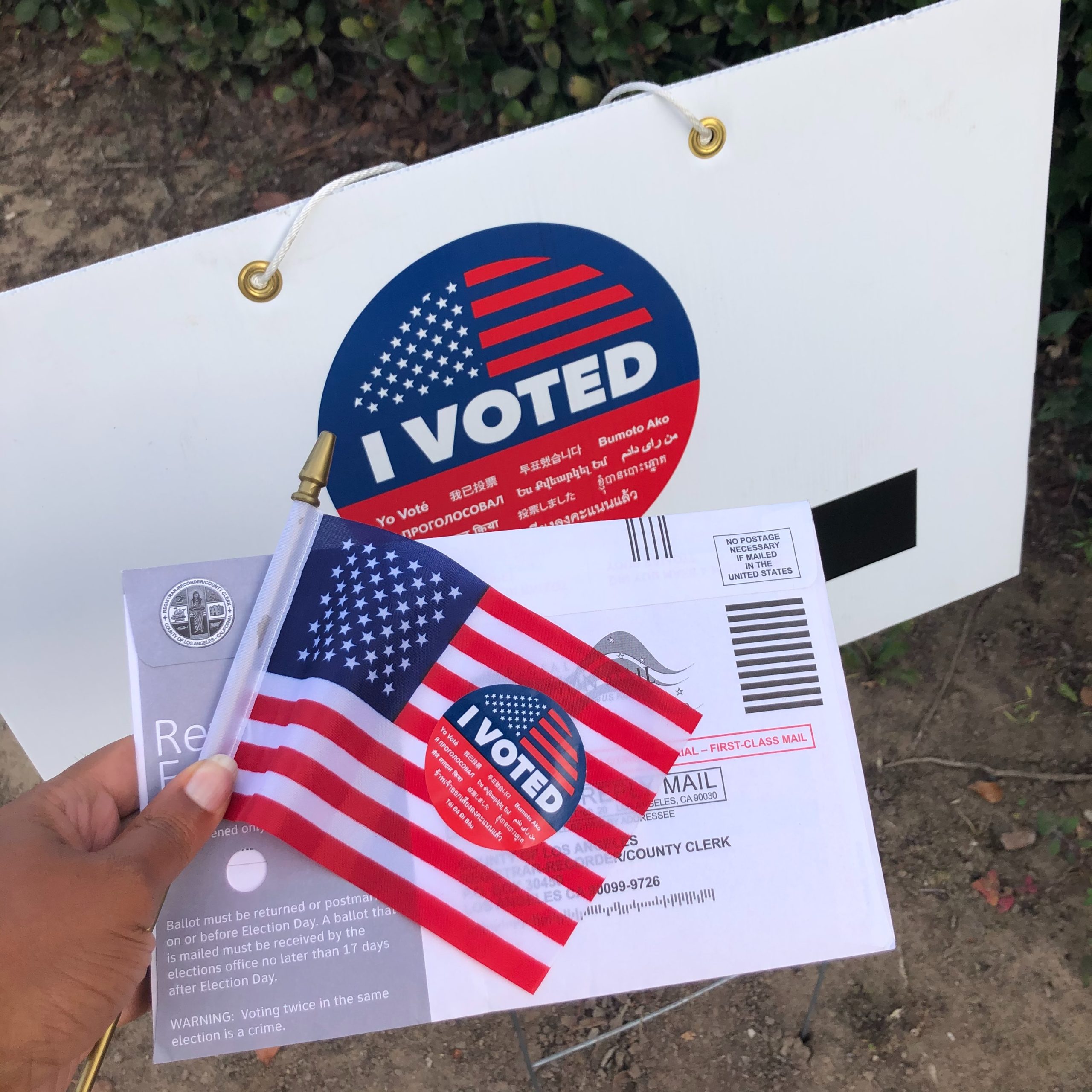 "I voted" sticker and sign with a mailed ballot and a small American flag