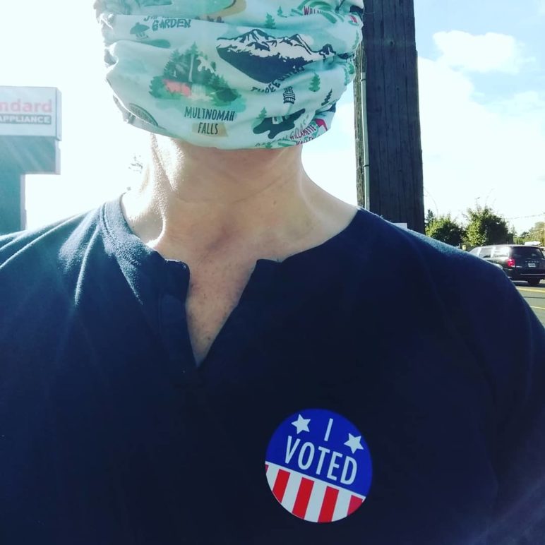 Person with an "I voted" sticker on their shirt and an Oregon-specific face mask