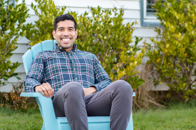 Profile photo of Sam Diaz sitting in a blue chair on the lawn of his white home