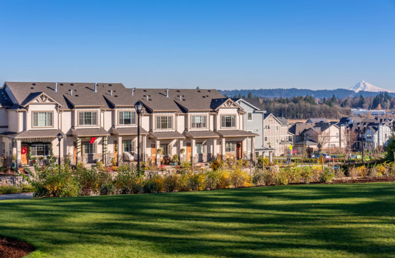 Row of tan townhouses with a green manicured lawn in the foreground, Mt. Hood in the background to the right