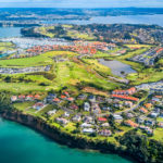 Aerial view of residential suburbs surrounded by sunny ocean harbor. Whangaparoa peninsula, Auckland, New Zealand