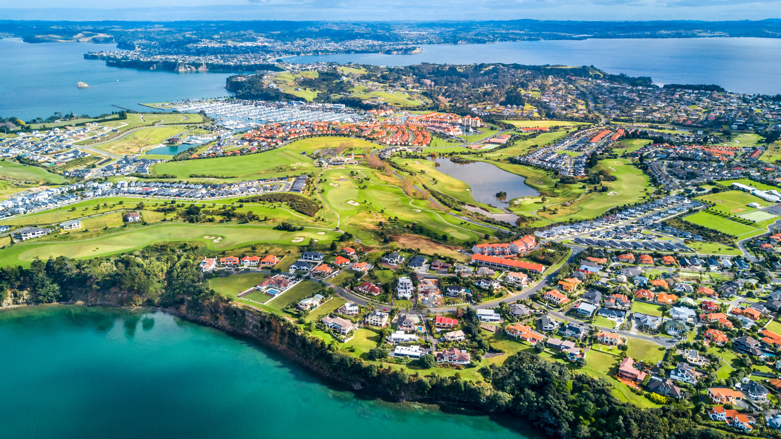 Aerial view of residential suburbs surrounded by sunny ocean harbor. Whangaparoa peninsula, Auckland, New Zealand