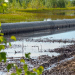 Photo of an oil pipeline laying along a green marsh.