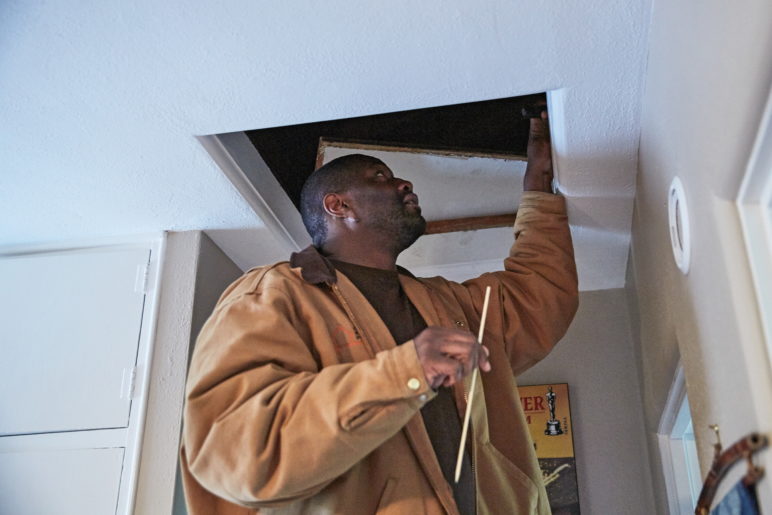 Photo of Community Energy Project staffperson looking up in an attic area for an efficiency project