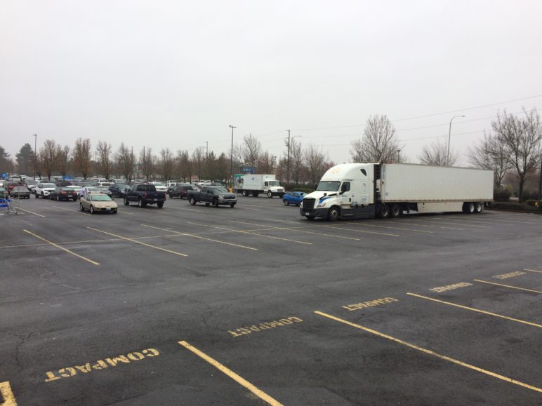 Photo of an empty Walmart parking lot. A few cars can be seen, including a shipping truck parked over several empty spots.