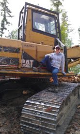 Photo of a person sitting against a CAT construction vehicle, resting on the treads.