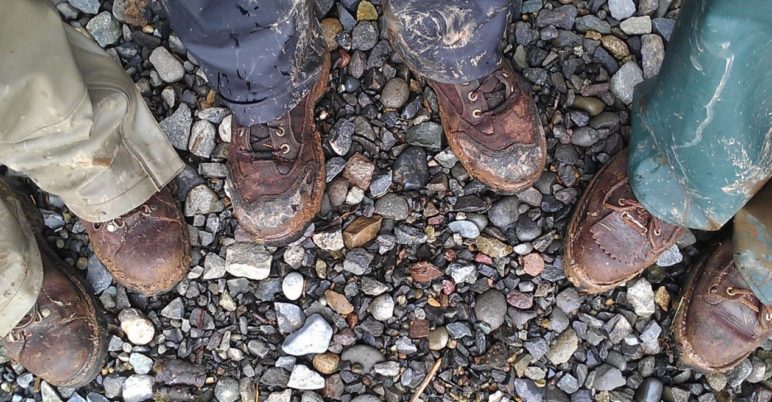 Close up of three people's brown boots on rocky gravel
