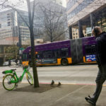 Man with headphones walking down city streets as a bike and bus is featured