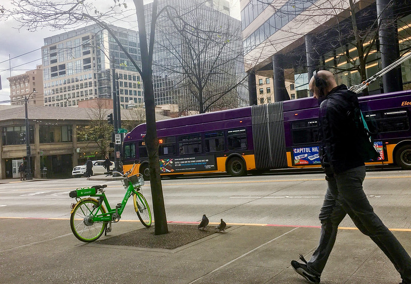 Man with headphones walking down city streets as a bike and bus is featured