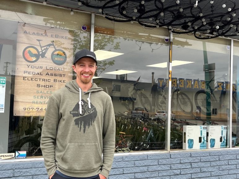 Photo of a young person smiling in front of a window of a bike shop