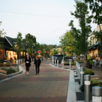 A pedestrianized commercial main street with attached one-story retail shops and a parked car outside.