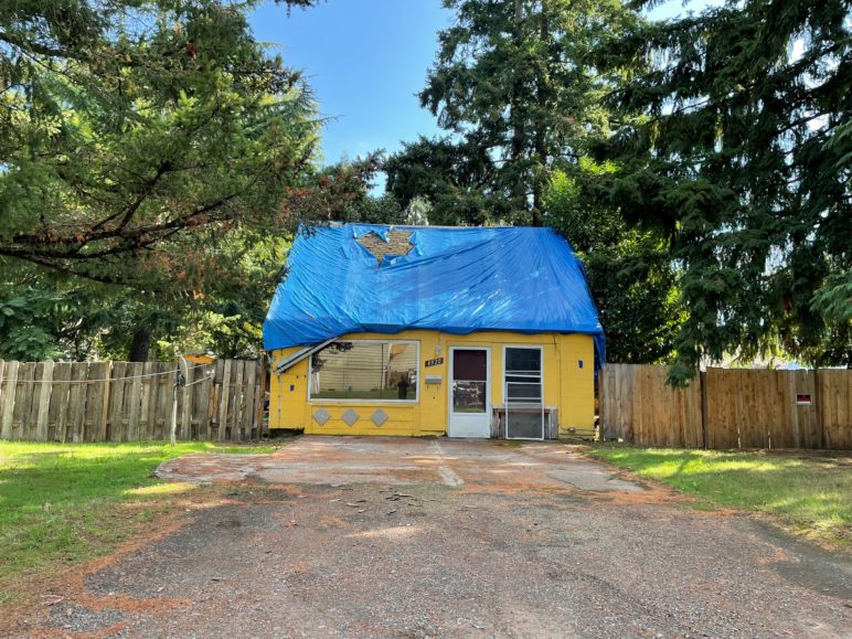 Thanks to Oregon’s parking reforms, 13 new homes will replace this decaying house with blue tarp over the roof on a dirt-road driveway. Photo by Gene Templeton. 
