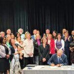 Housing abundance bills signed by Governor Inslee in Washington state in 2023. Inslee signs while surrounded by a crowd of advocates.