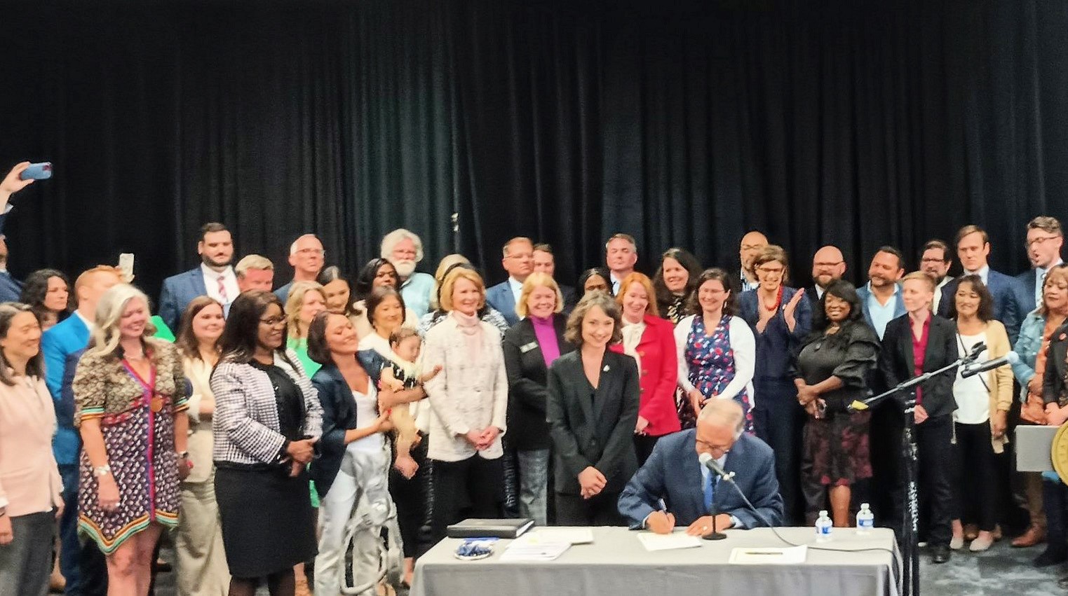 Housing abundance bills signed by Governor Inslee in Washington state in 2023. Inslee signs while surrounded by a crowd of advocates.