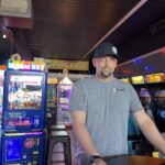 Photo of a goatee'd person in a grey shirt and black cap inside a video arcade