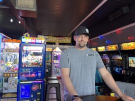 Photo of a goatee'd person in a grey shirt and black cap inside a video arcade