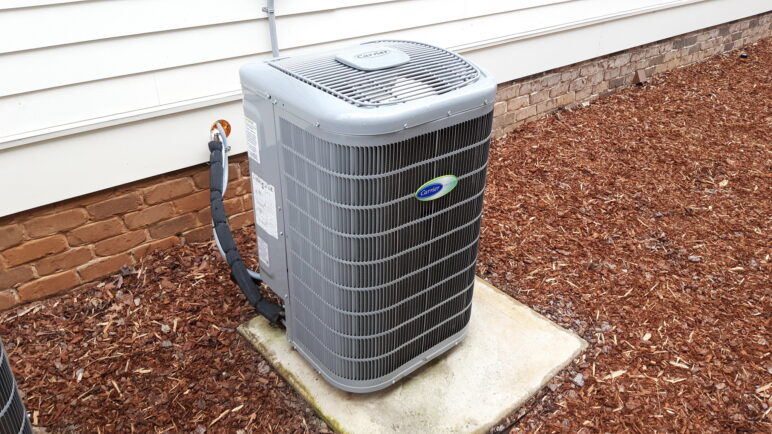 Photo of a heat pump next to a white wall on top of wood bark