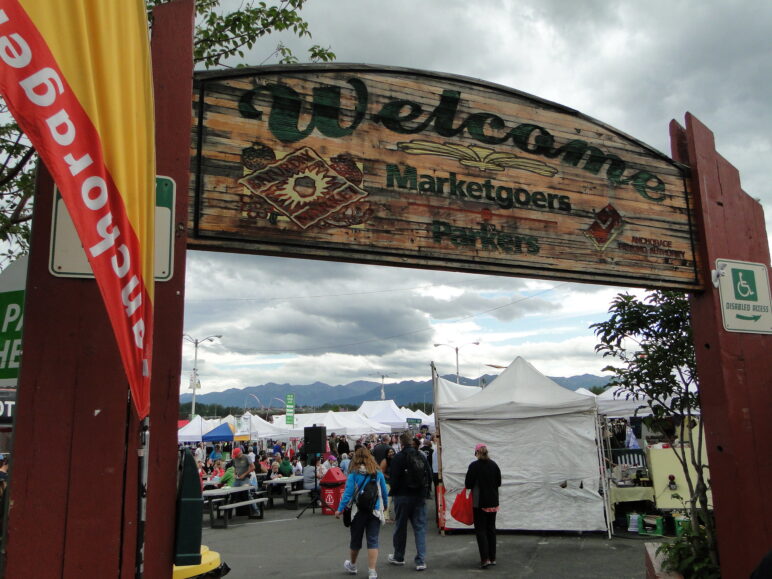 Anchorage Saturday Market by Amy Meredith used under CC BY-ND 2.0 (https://www.flickr.com/photos/jjandames/9464563966/) Large wooden "Welcome" sign leading to the Anchorage market held in a parking lot