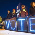 People holding a light up sign that spells out VOTE at night