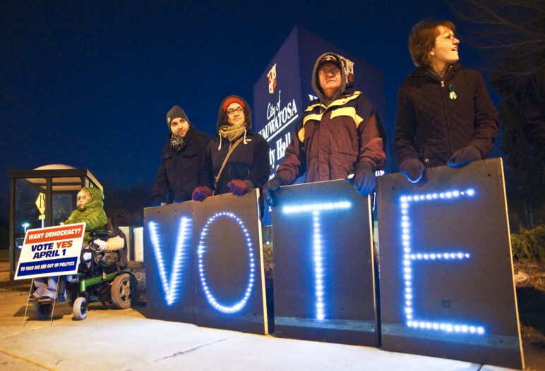 People holding a light up sign that spells out VOTE at night