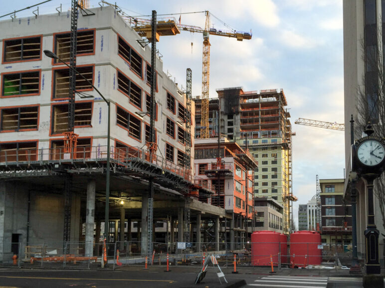 Photo of construction in a downtown area, with cranes and frames visible on a clear day.