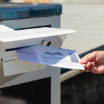 Photo of someone tossing their mail-in ballot into the mailbox