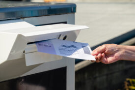 Photo of someone tossing their mail-in ballot into the mailbox