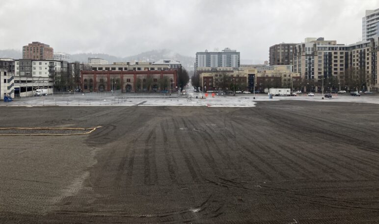 photo of a large muddy field with the high-rises of Portland's Pearl district visible behind it.