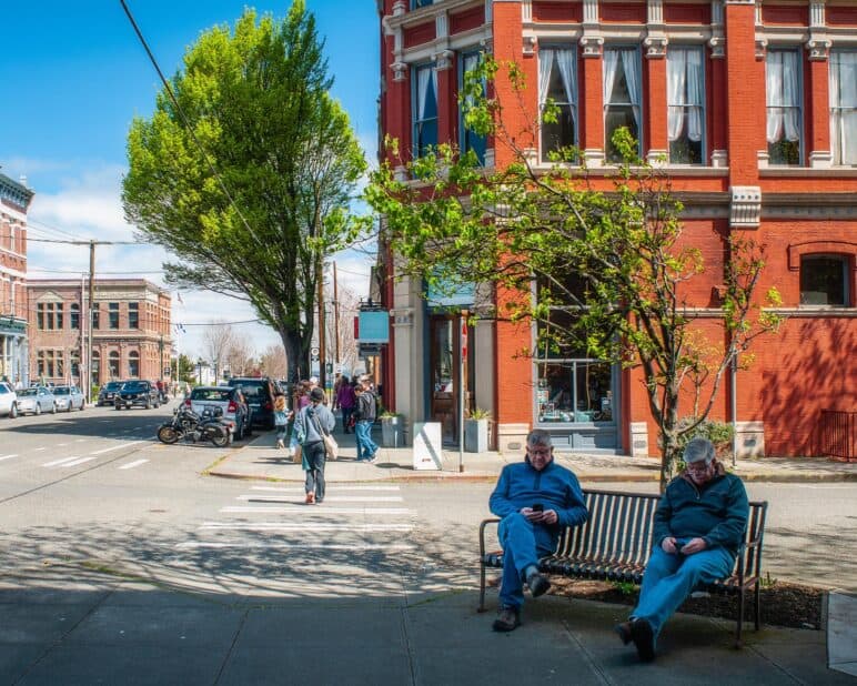 April 20, 2019: A scene on Water Street in Historic Port Townsend, Washington. 2 older men checking social media
