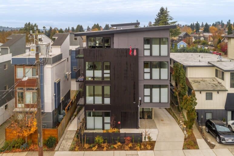 Photograph courtesy of BUILD LLC. Aerial photo with a focus on a 4-story apartment building on a city street. Large-pane windows can be seen on the sides on an autumn day.