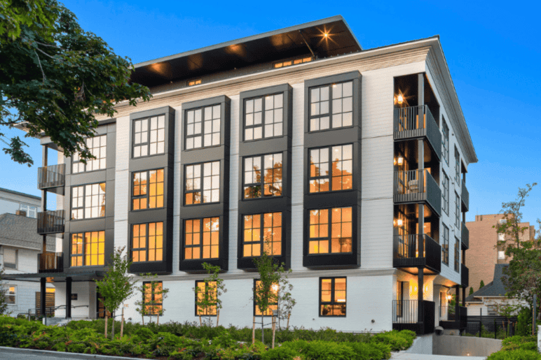 Photograph courtesy of Steve Snider/Real Residential. Photo of a four-story multi-unit building. Large windows make up the sides of the building, and private corner decks can be seen on each floor.