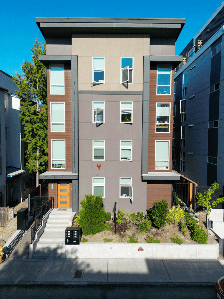 Photograph by Alex Hart Photography. Photograph of a narrow multi-unit building on a city lot. A simple garden on the ground floor leads to the front door.