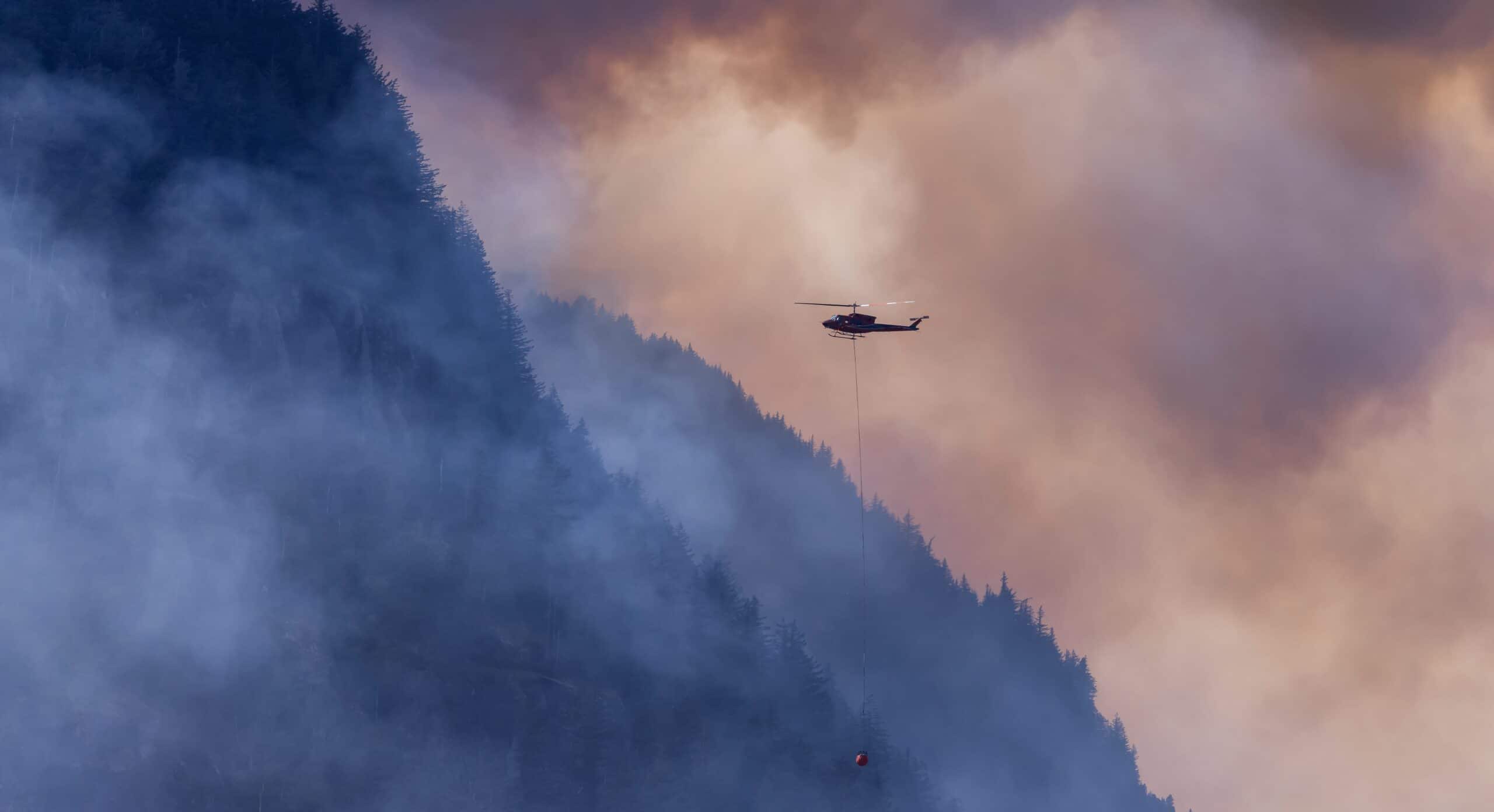 A wildfire service helicopter flies over fire and smoke near Hope, BC, during wildfires in 2022. The area, about two hours east of Vancouver, was evacuated again during 2025 fires. Photo by EB Adventure Photography. 
