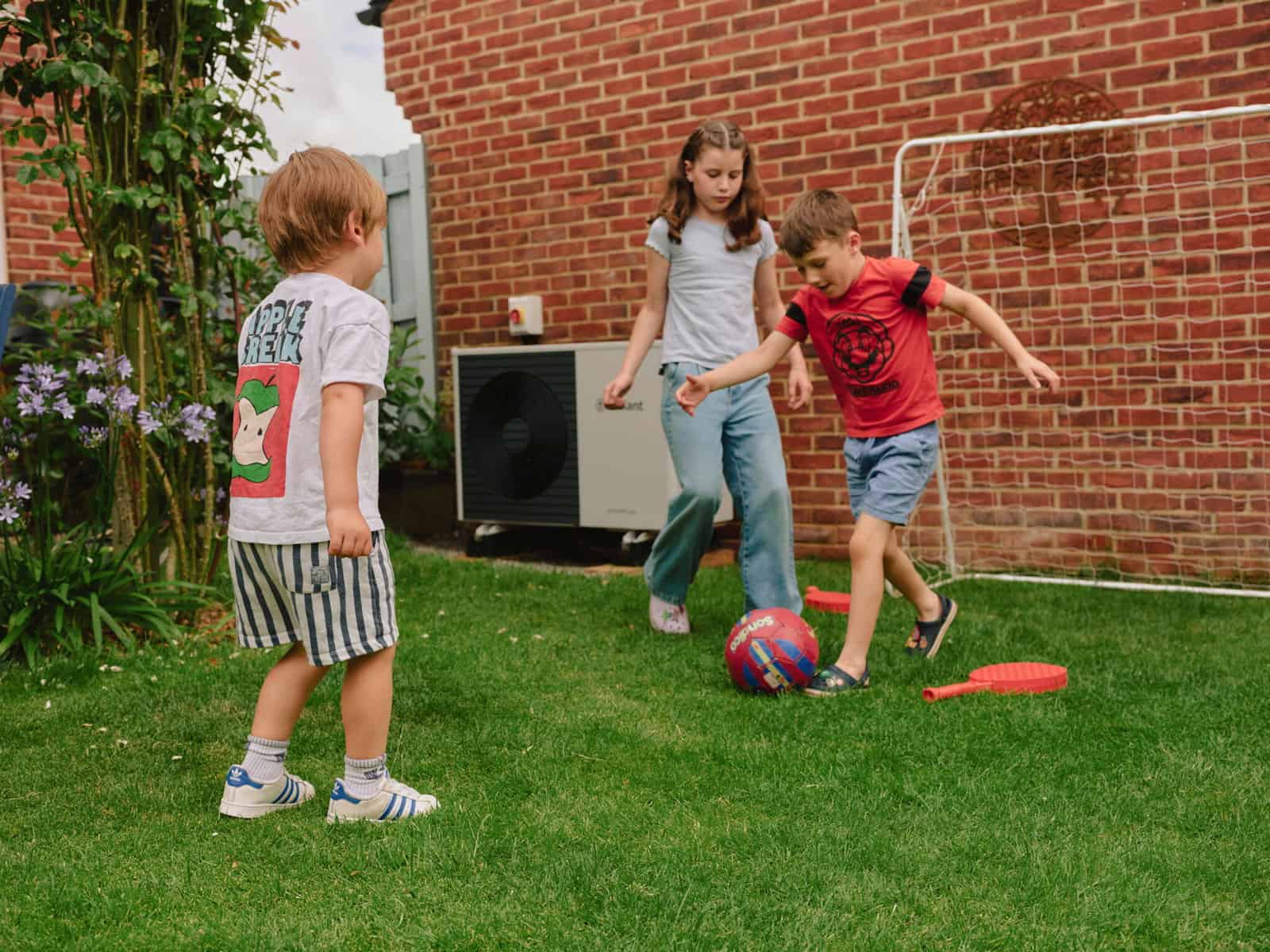 Children play in a backyard near a visible heat pump. Some Cascadian HOAs or "community associations” ban heat pumps explicitly or impose rules that prevent installation. Photo by Liz Seabrook / Nesta for Climate Visuals.